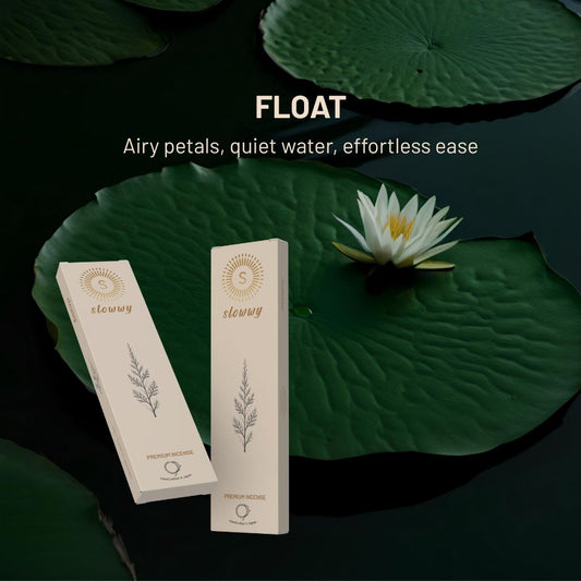 Two cream-colored slowwy brand product boxes are displayed on a dark water background with large green lily pads and a white water lily flower. White text at the top reads 'FLOAT' and 'Airy petals, quiet water, effortless ease'.